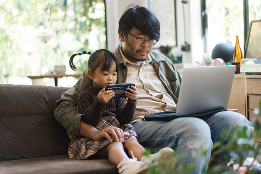 Dad and daughter sitting on a sofa looking at a laptop